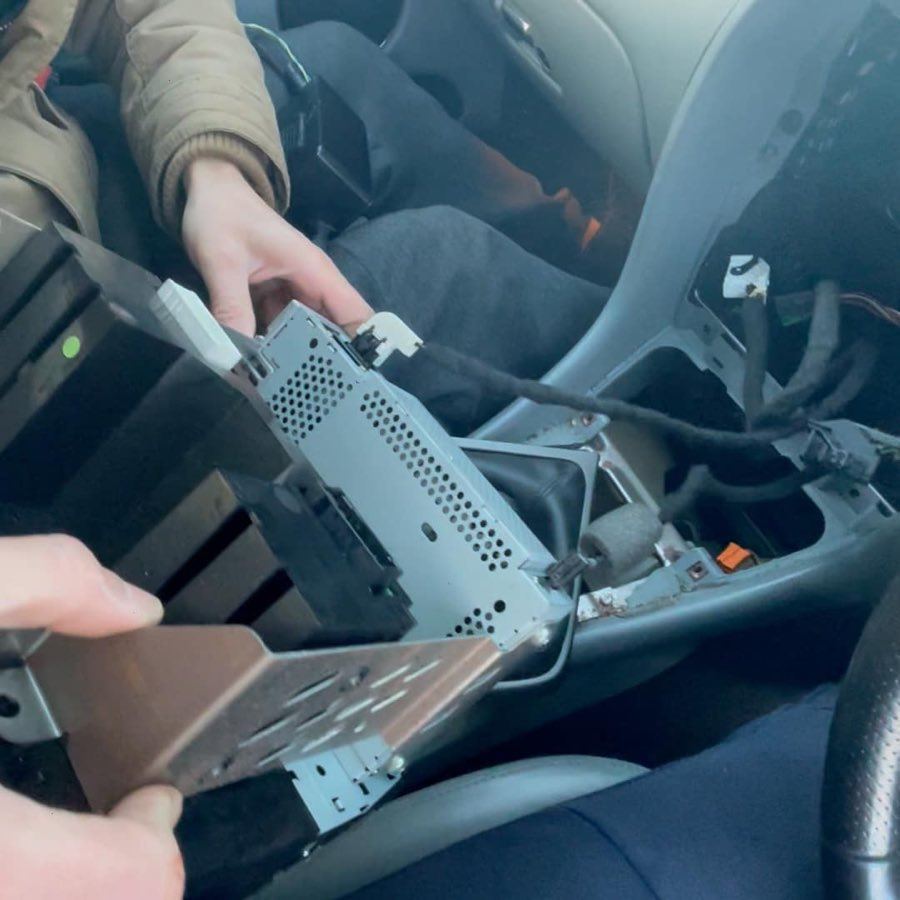 The stereo being drawn out of the centre console of a Jaguar, connectors visible behind it